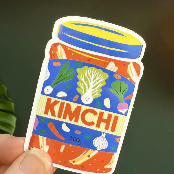 Naomi Wilkinson sticker of a jar of kimchi with smiling vegetables, held in a hand