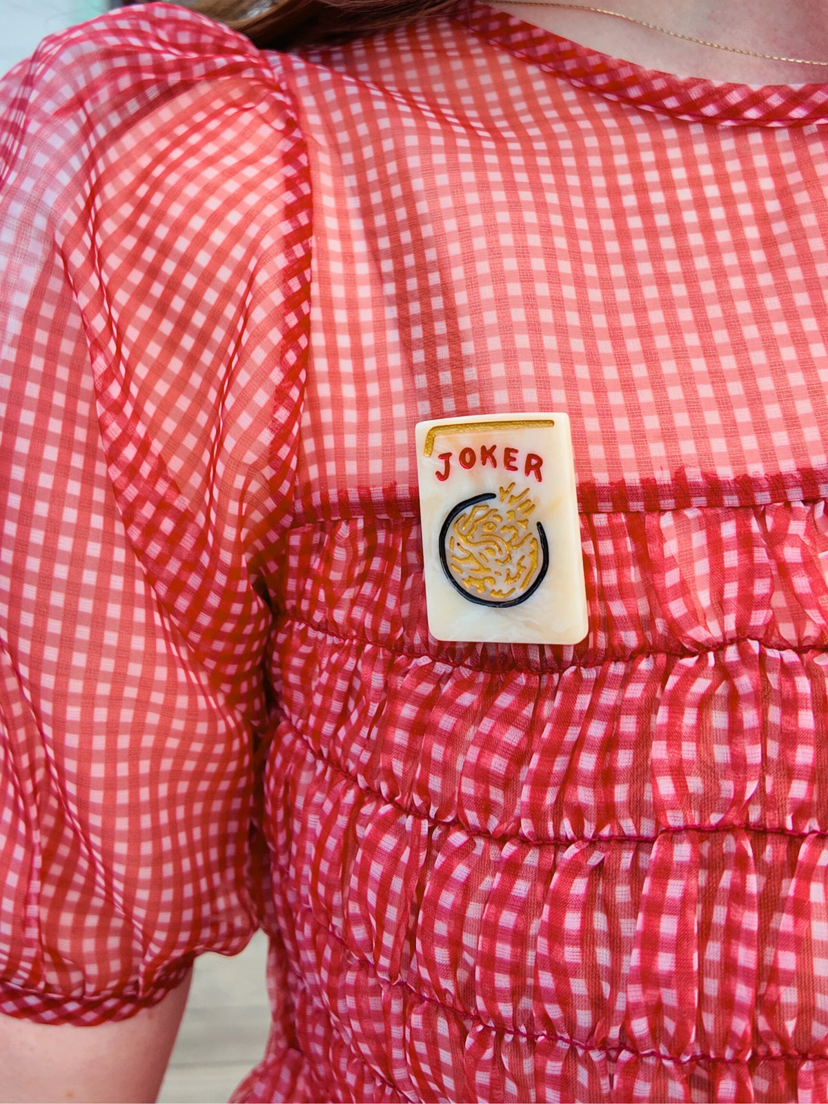 Solar Eclipse mahjong tile brooch reading 'Joker', on a red gingham blouse