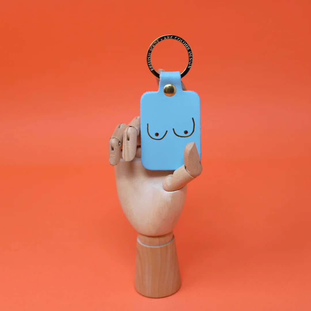 Turquoise leather key fob printed with a pair of boobs, held by a wooden hand