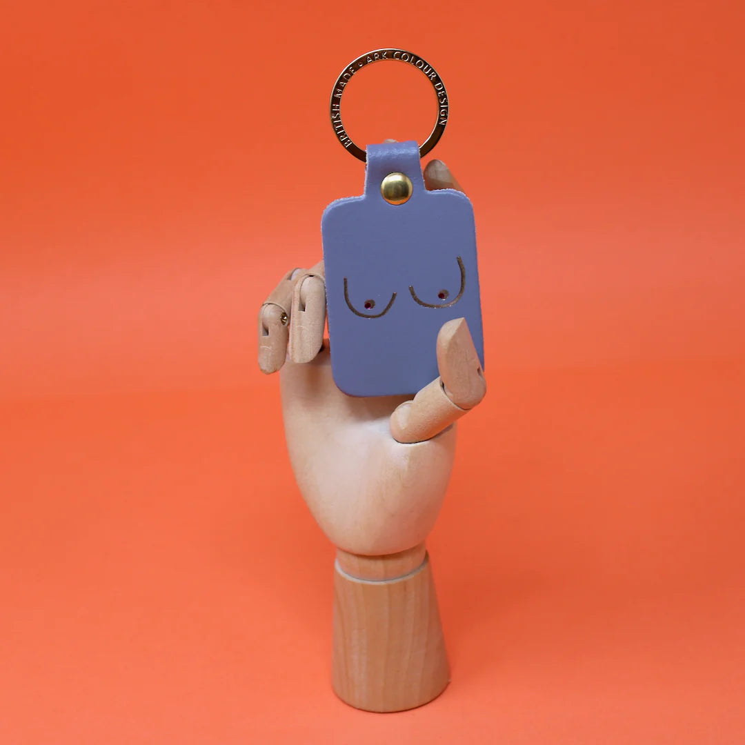 Ark lilac grey leather key fob with a line drawing of boobs, held by a wooden hand