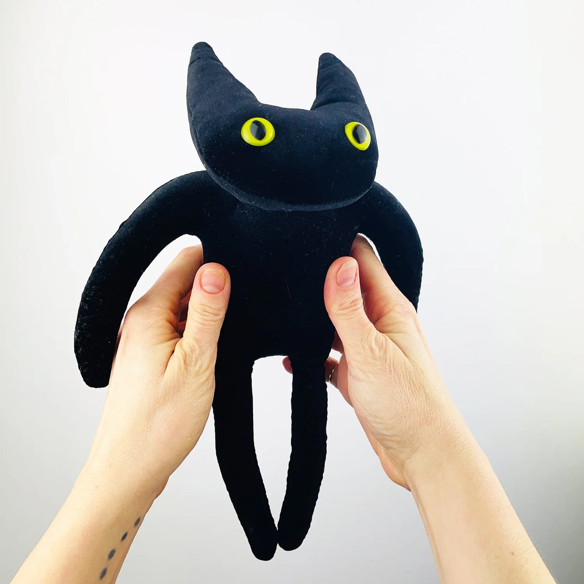 Hands holding a navy blue cat soft toy with long legs and yellow eyes