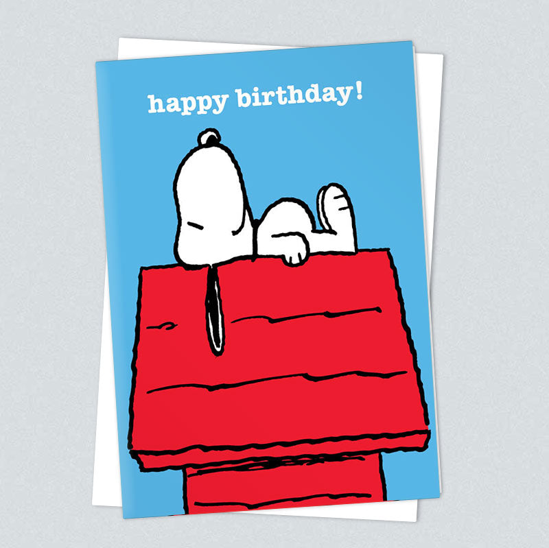Blue card of Snoopy lying on his red kennel: happy birthday!