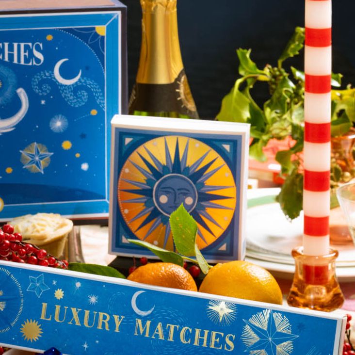 Golden blue sun matchbox on a festive table with oranges and candles