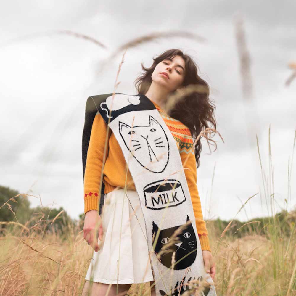 Woman in a field wearing the black mog scarf with a milk bottle design