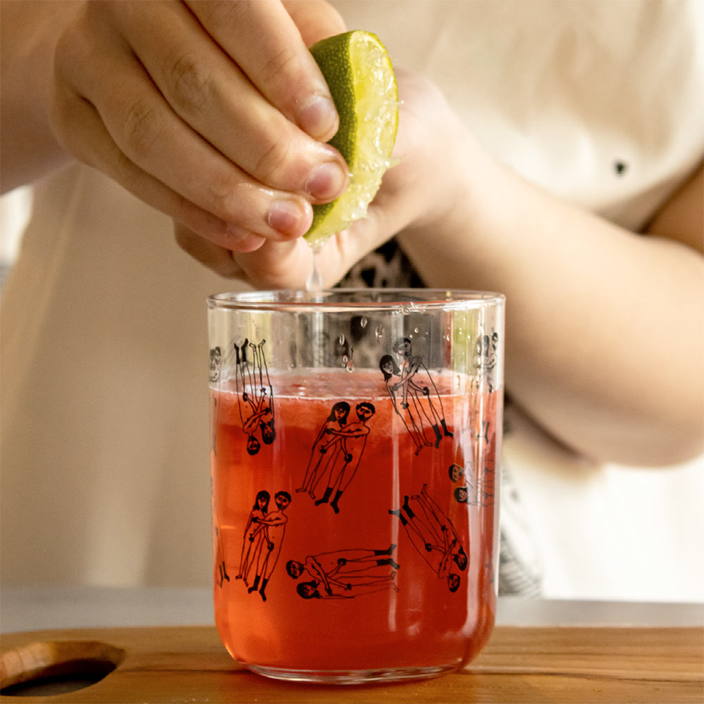 Lime being squeezed into a naked couple tumbler of pink drink