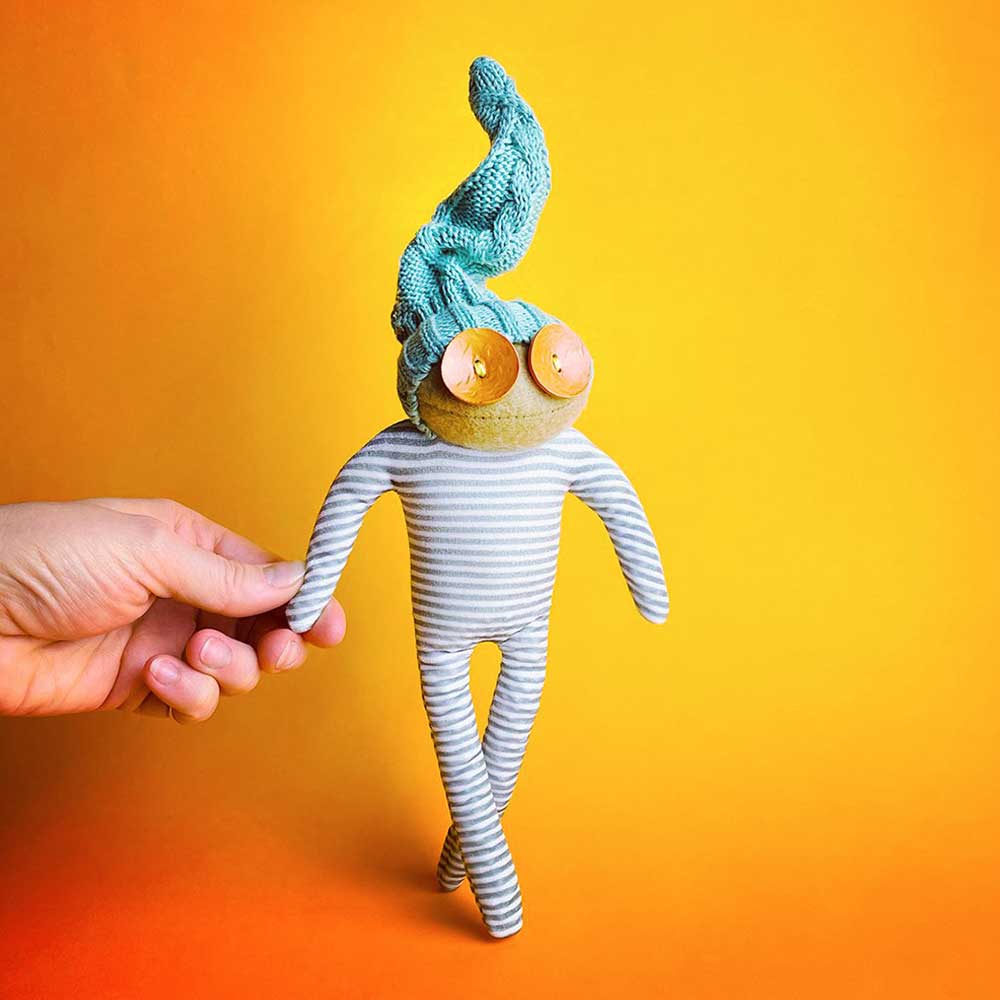 Small striped knitted doll with blue hair and big button eyes, held up against orange