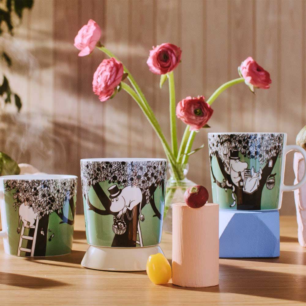 Green Moomin mugs on a table with pink flowers