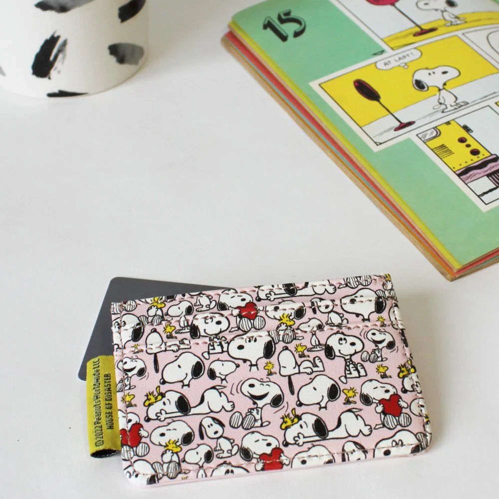 Patterned back of the pink Snoopy card holder holding a card, beside a Peanuts comic book