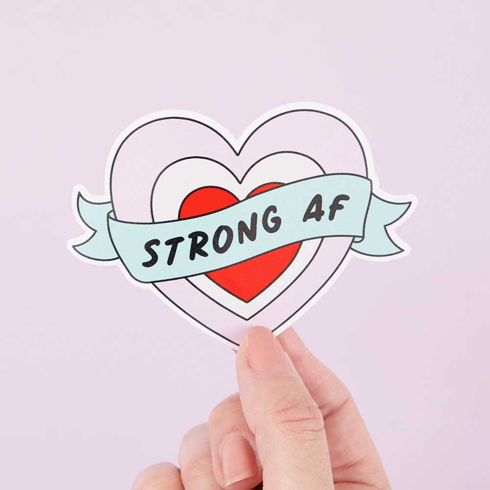 Hand holding a heart sticker with a banner: Strong AF