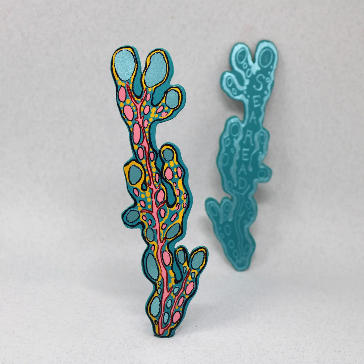 Pair of seaweed-shaped leather bookmarks, one patterned in pink and yellow, one turquoise