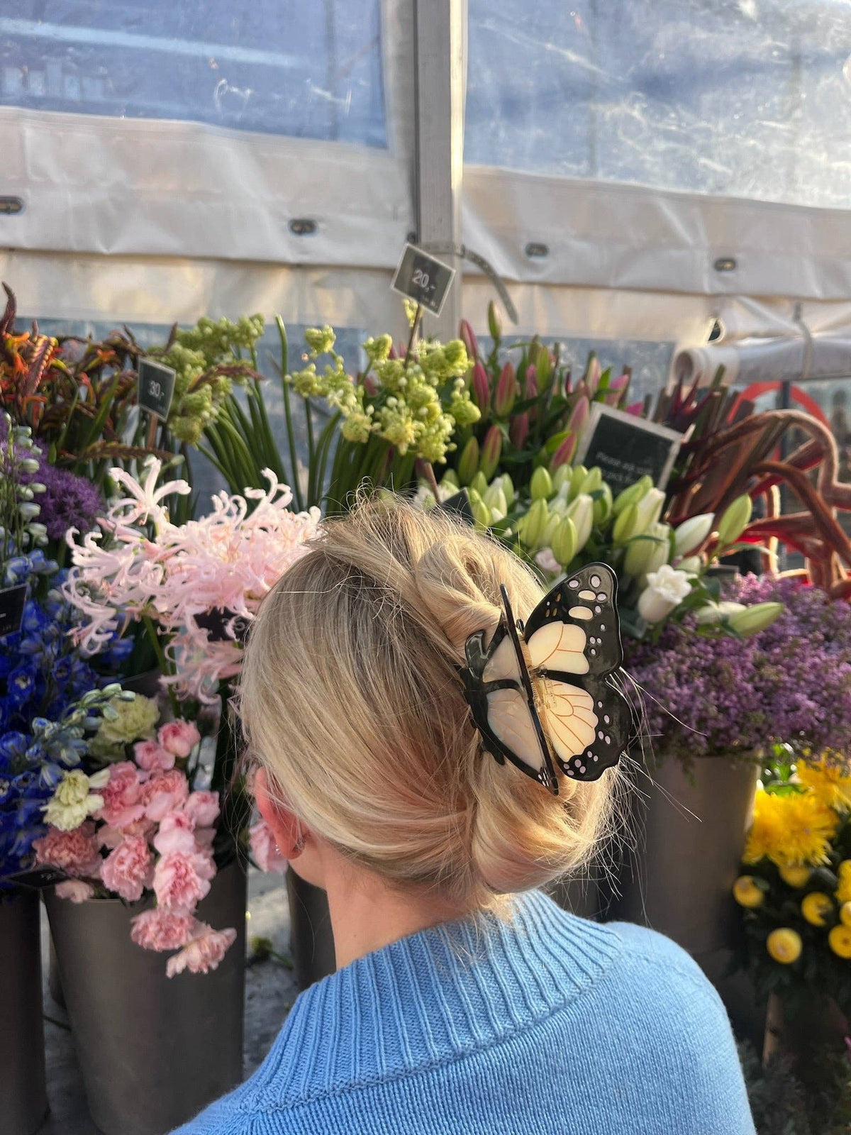 Blonde hair held up with a black butterfly claw clip beside a flower stall
