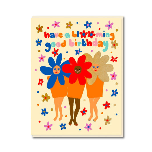 Card with three women with flower heads among scattered flowers: have a blooming good birthday