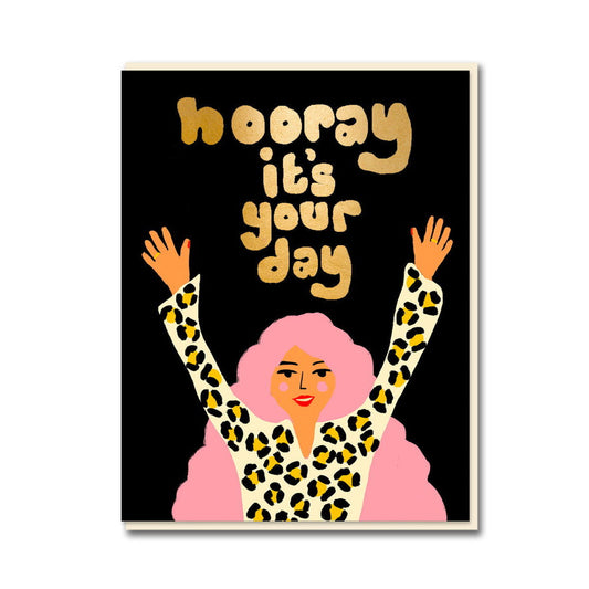 1973 card: a woman with pink hair in a leopard print coat throwing her arms up, with gold 'Hooray it's your day' on black