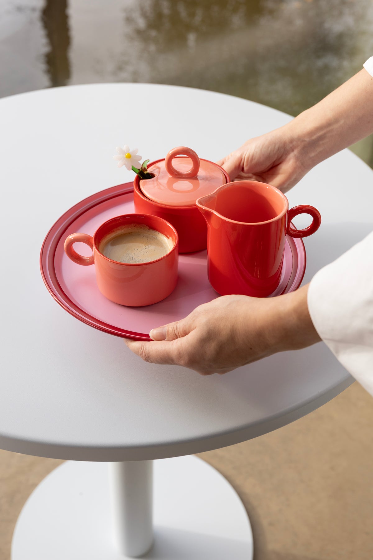 Hands holding a red tray with the red Chiquito milk jug and cups