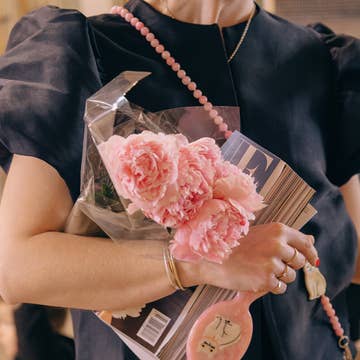 Pink cat hairbrush hanging from a bag strap beside pink peonies
