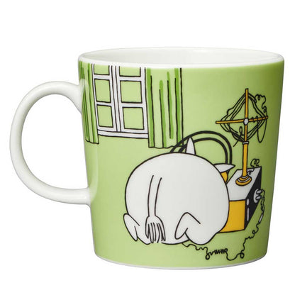 Other side of the grass green mug: Moomintroll crouching beside a house with a pan