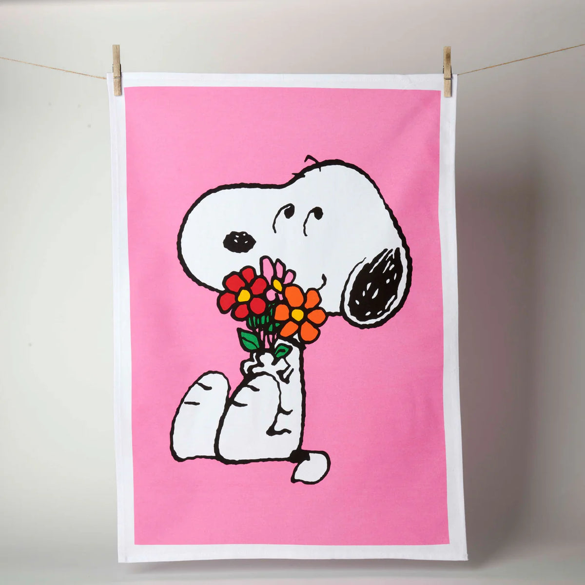 Pink tea towel with Snoopy holding a bunch of flowers, pegged on a line