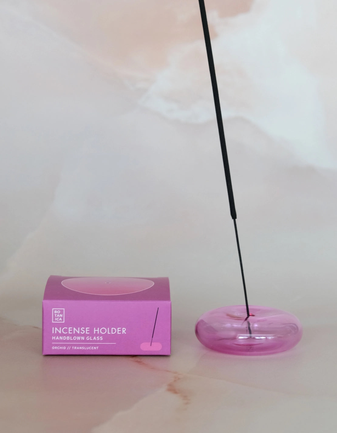 Lit incense stick in the orchid pink glass holder, next to its box