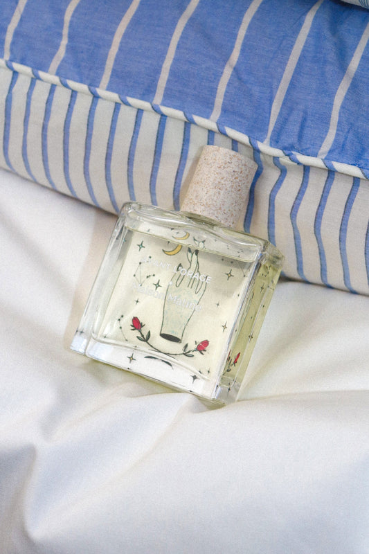 Maison Matine Avant l'Orage perfume, 50ml, on white bedding beside a striped pillow