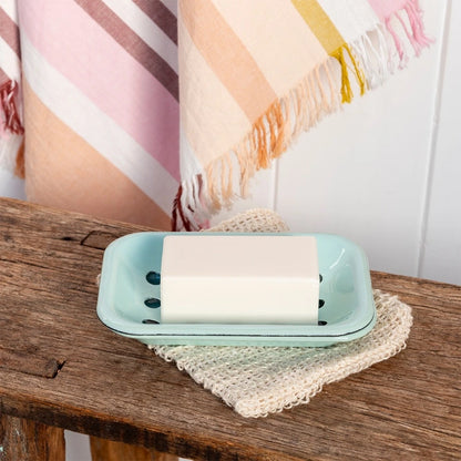 Turquoise enamel soap dish holding a bar of soap on a wooden bench