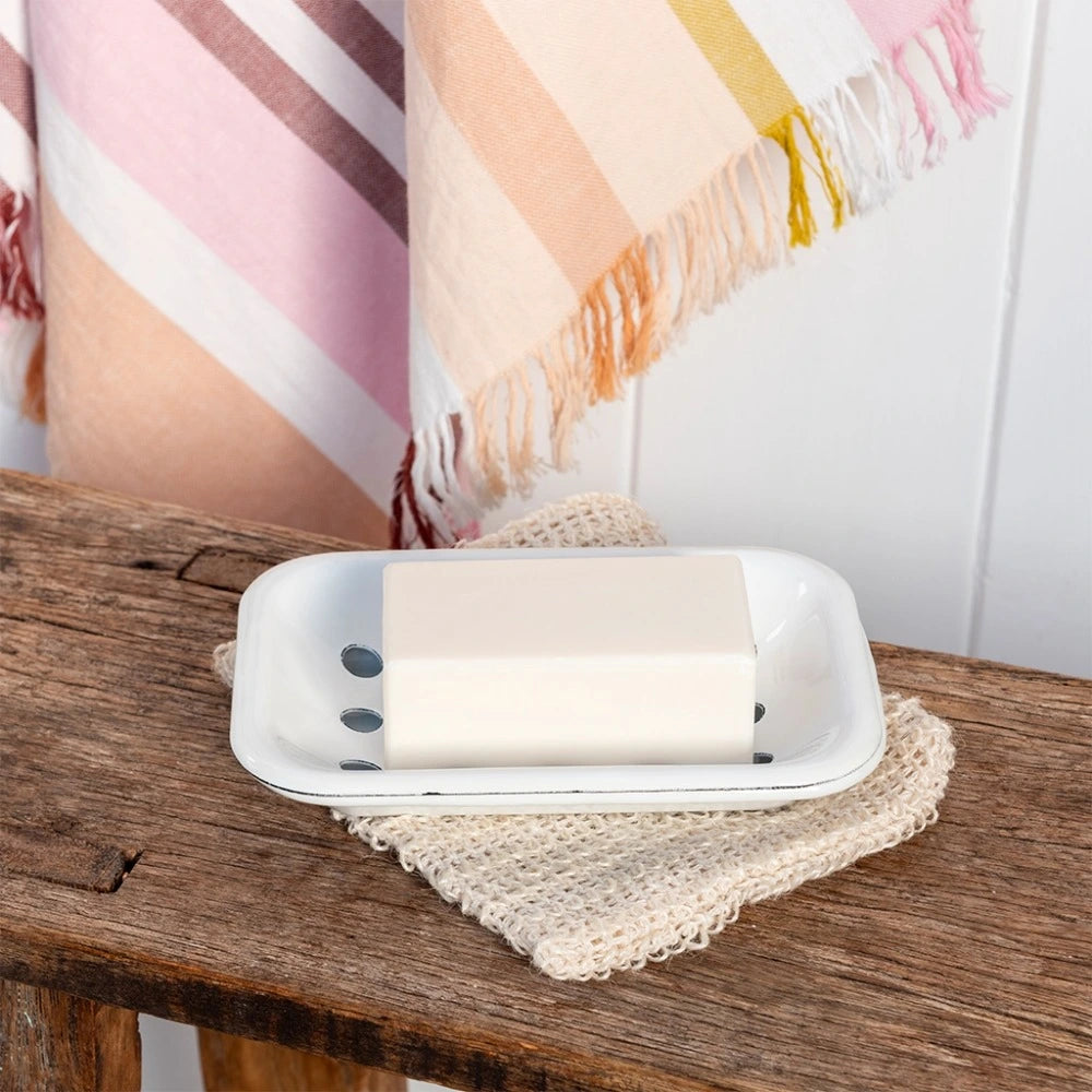 White enamel soap dish holding a bar of soap on a wooden bench