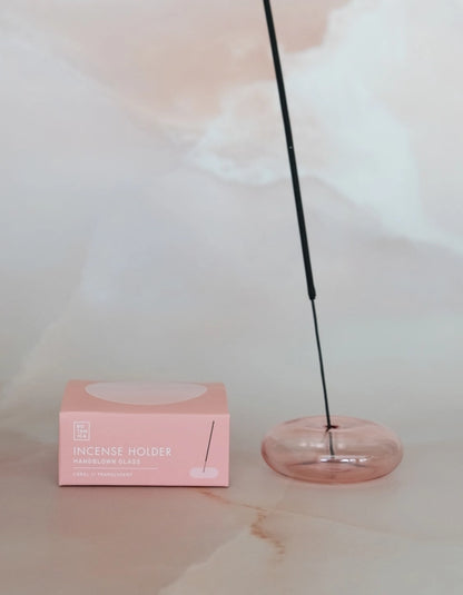 Incense stick burning in the coral glass holder beside its pink box