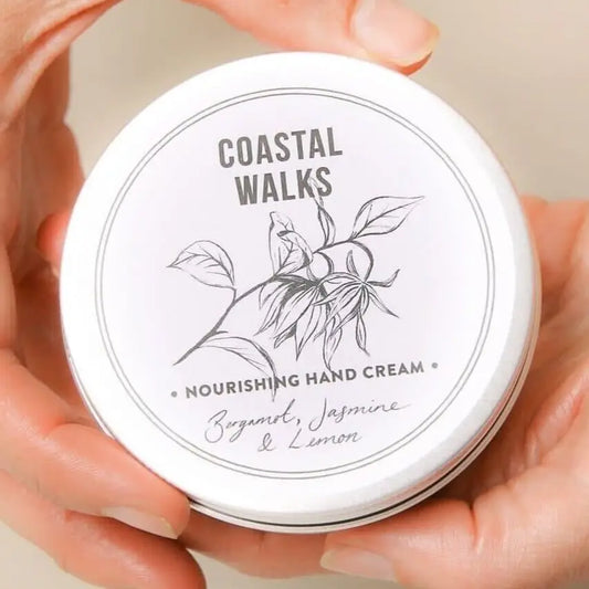 Hands holding a Norfolk Natural Living Coastal Walks hand cream 100ml tin