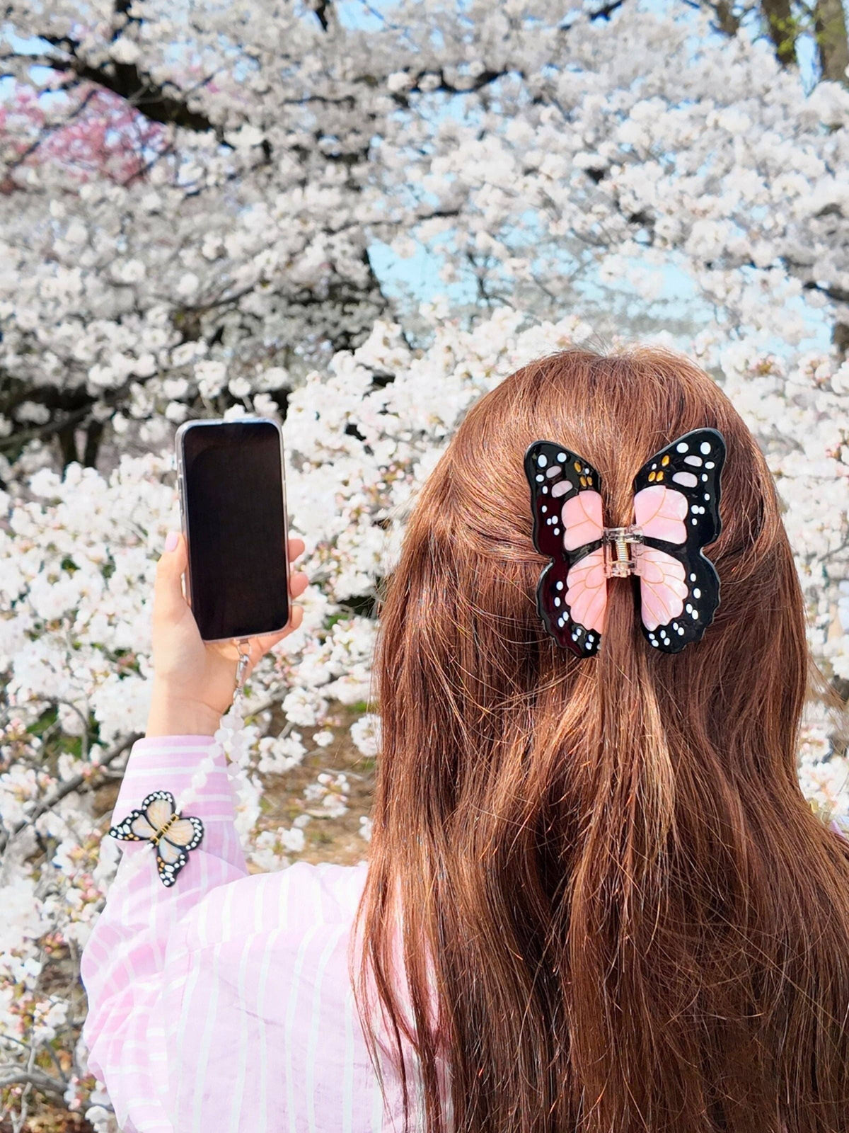 Woman with a phone wearing the pink butterfly clip under cherry blossom