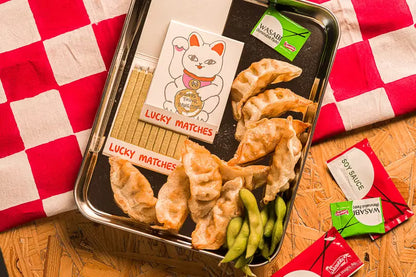 Lucky Cat matches on a tray of dumplings and edamame on a red check cloth