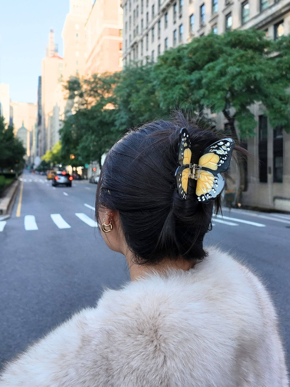 Orange monarch clip in dark hair on a city street, woman in a fur coat