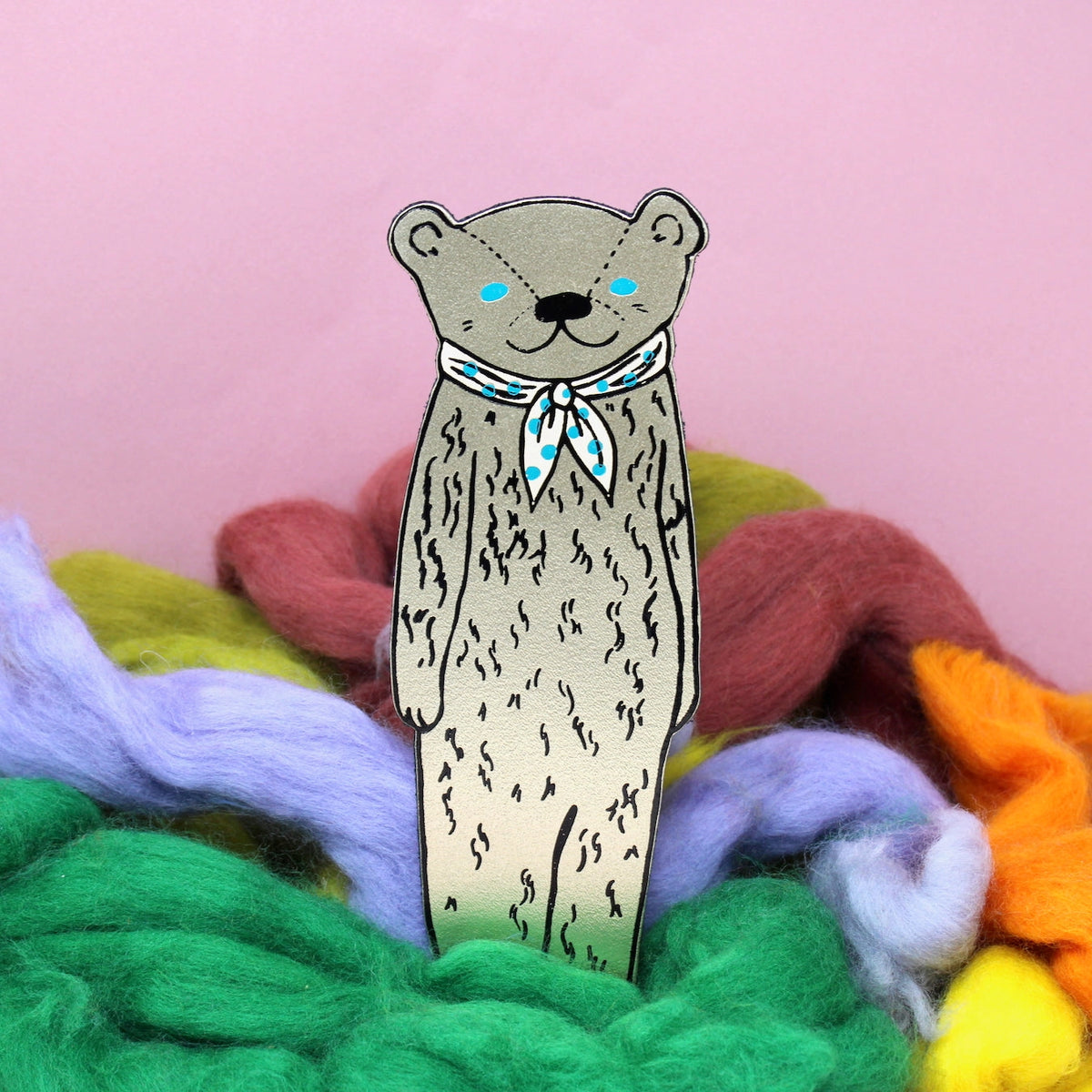 Ark gold bear bookmark wearing a blue neckerchief, among coloured wool