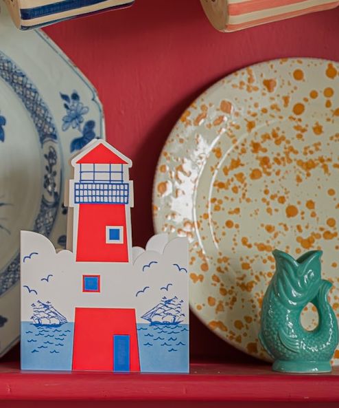 Lighthouse card standing on a shelf beside patterned plates