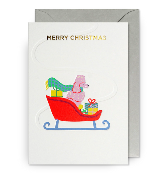 Lagom card: a pink poodle in a red sleigh with presents, with gold 'Merry Christmas'