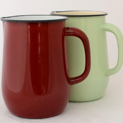 Dark red enamel jug in front of a pale green one