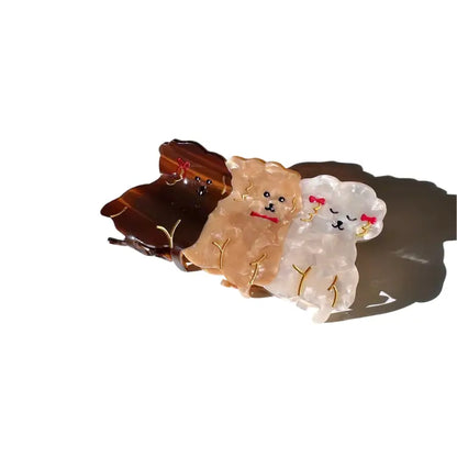 Claw hair clip of two fluffy puppies, one tan and one white, on a tortoiseshell clip
