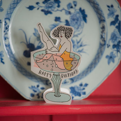 The cocktail cut-out card standing in front of a blue and white plate