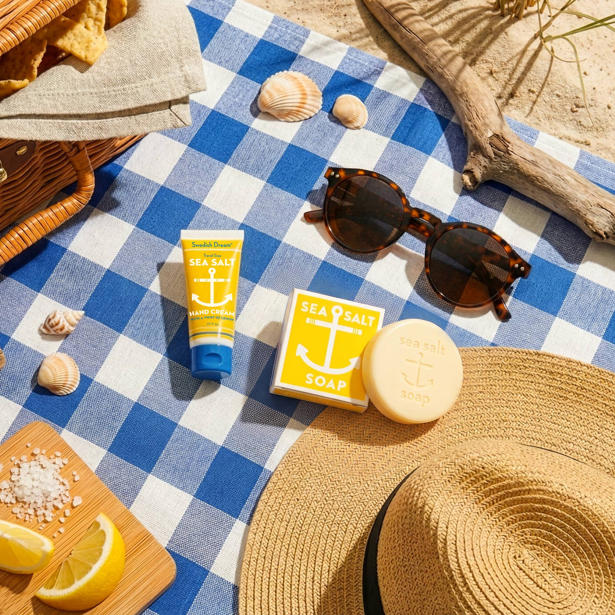 Sea salt soap and hand cream on a gingham picnic blanket with sunglasses and lemons