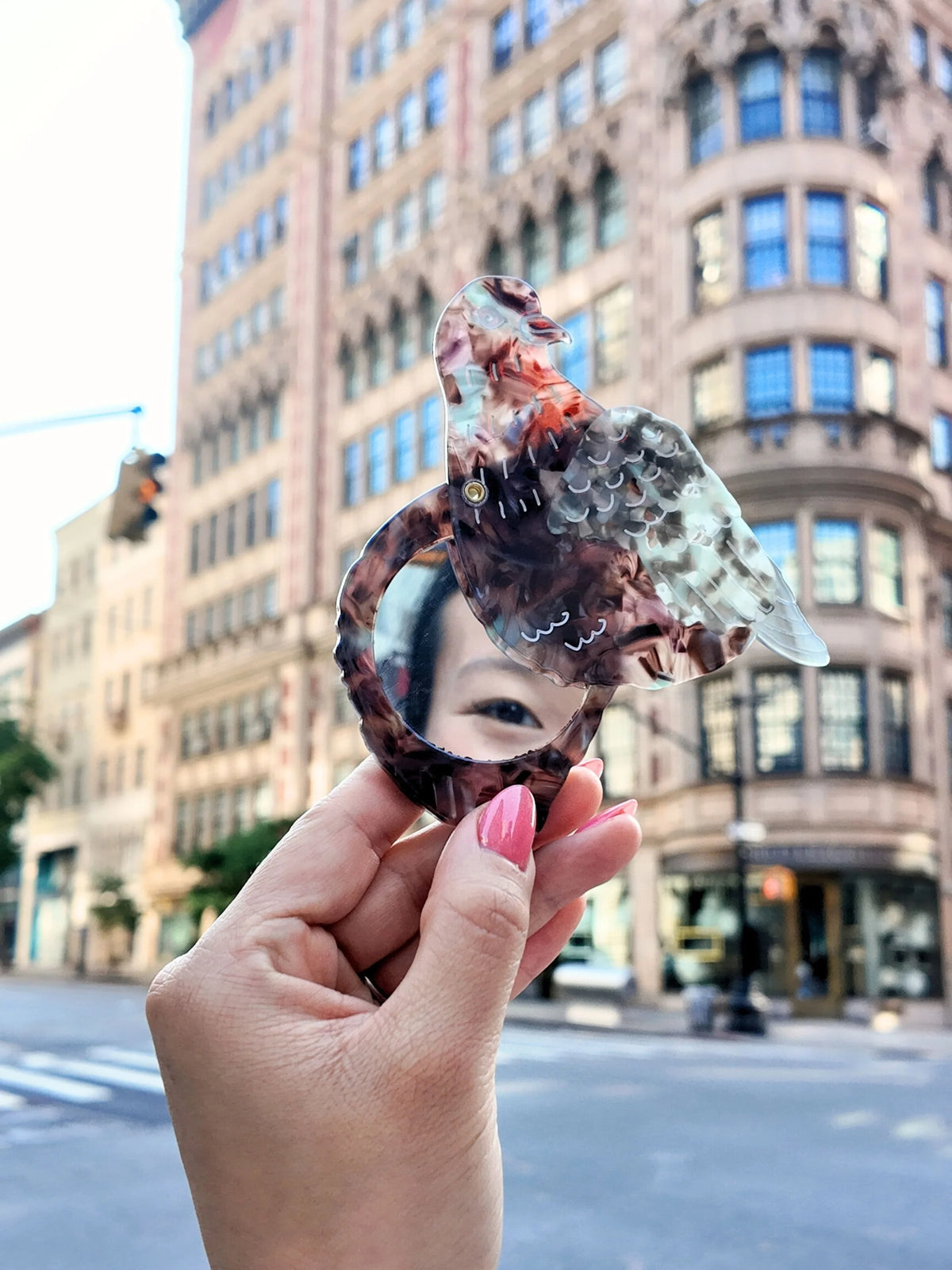 Hand holding the open pigeon compact mirror on a city street