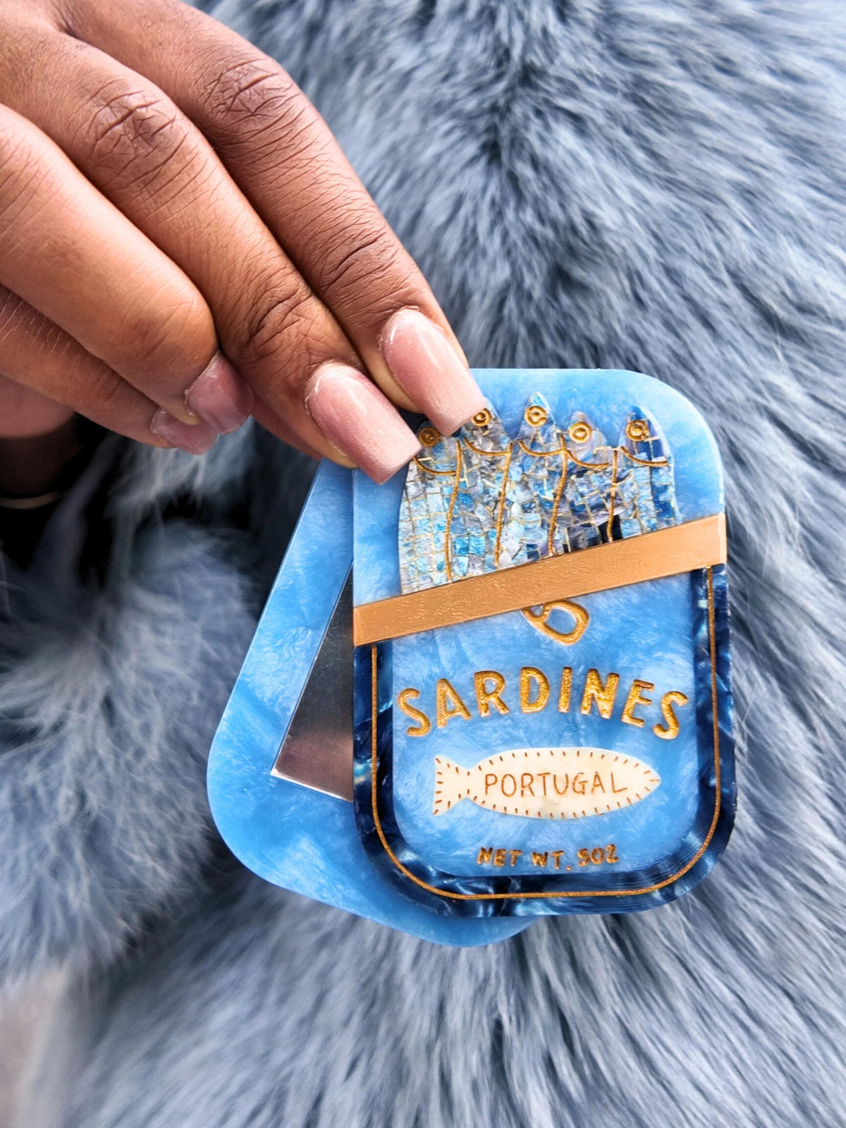 Hand holding the sardine tin compact mirror over grey fur