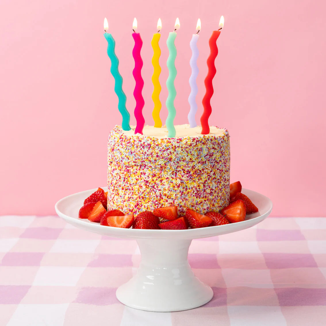 Sprinkle-covered cake topped with lit wavy candles