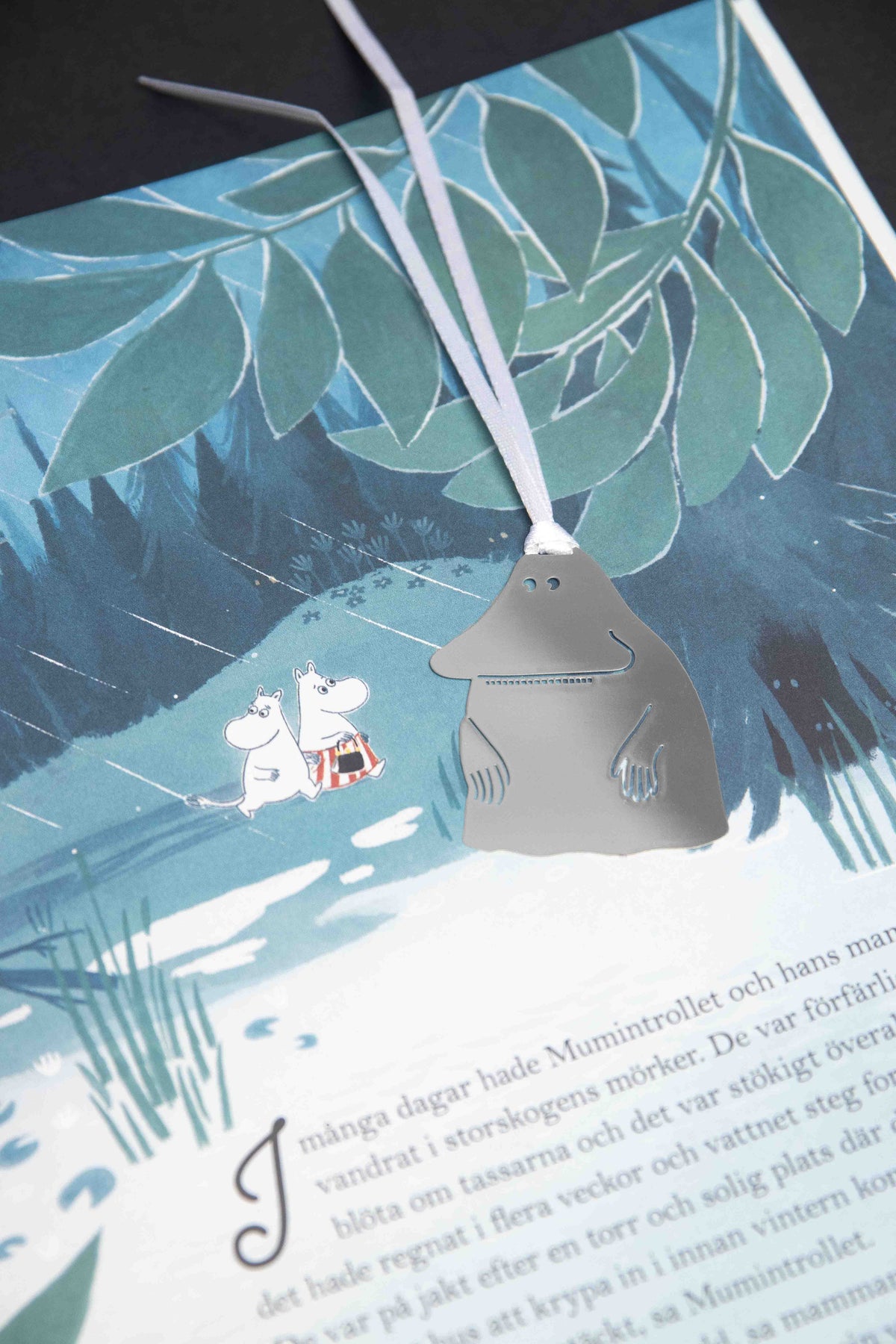 Groke bookmark lying on an illustrated Moomin book page