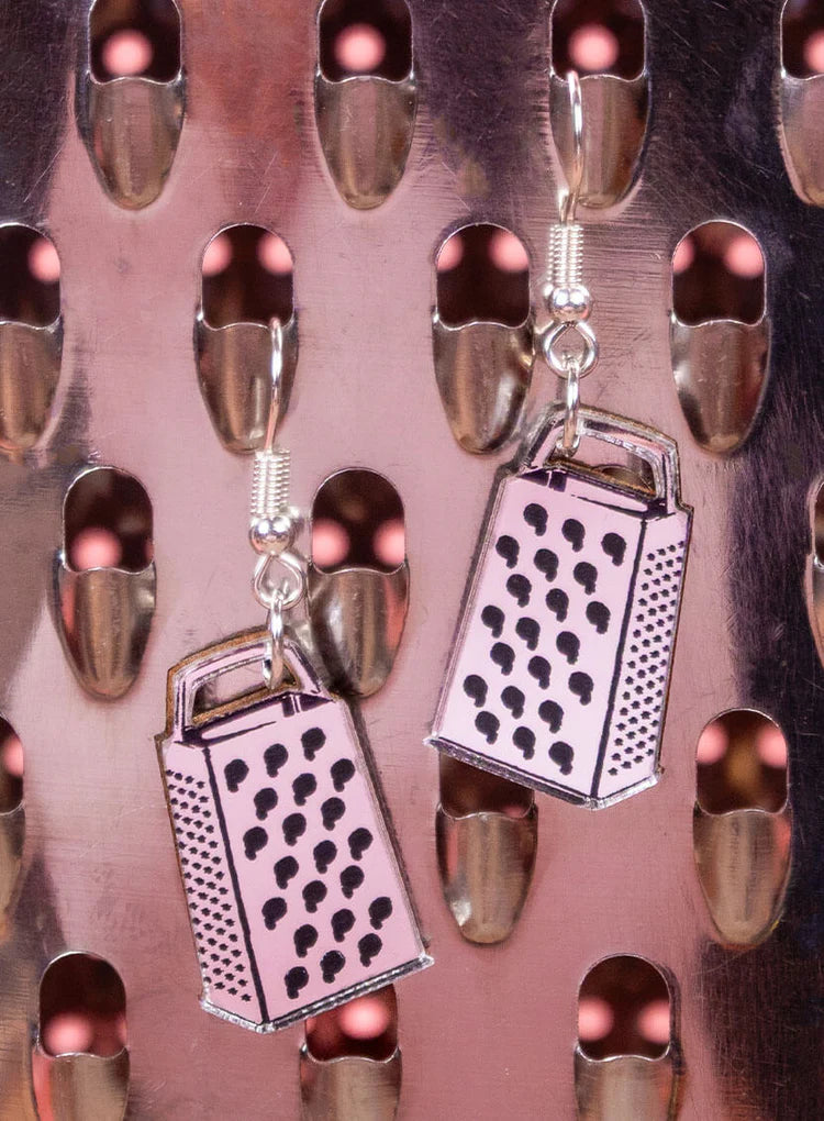 Cheese grater earrings on a pink background