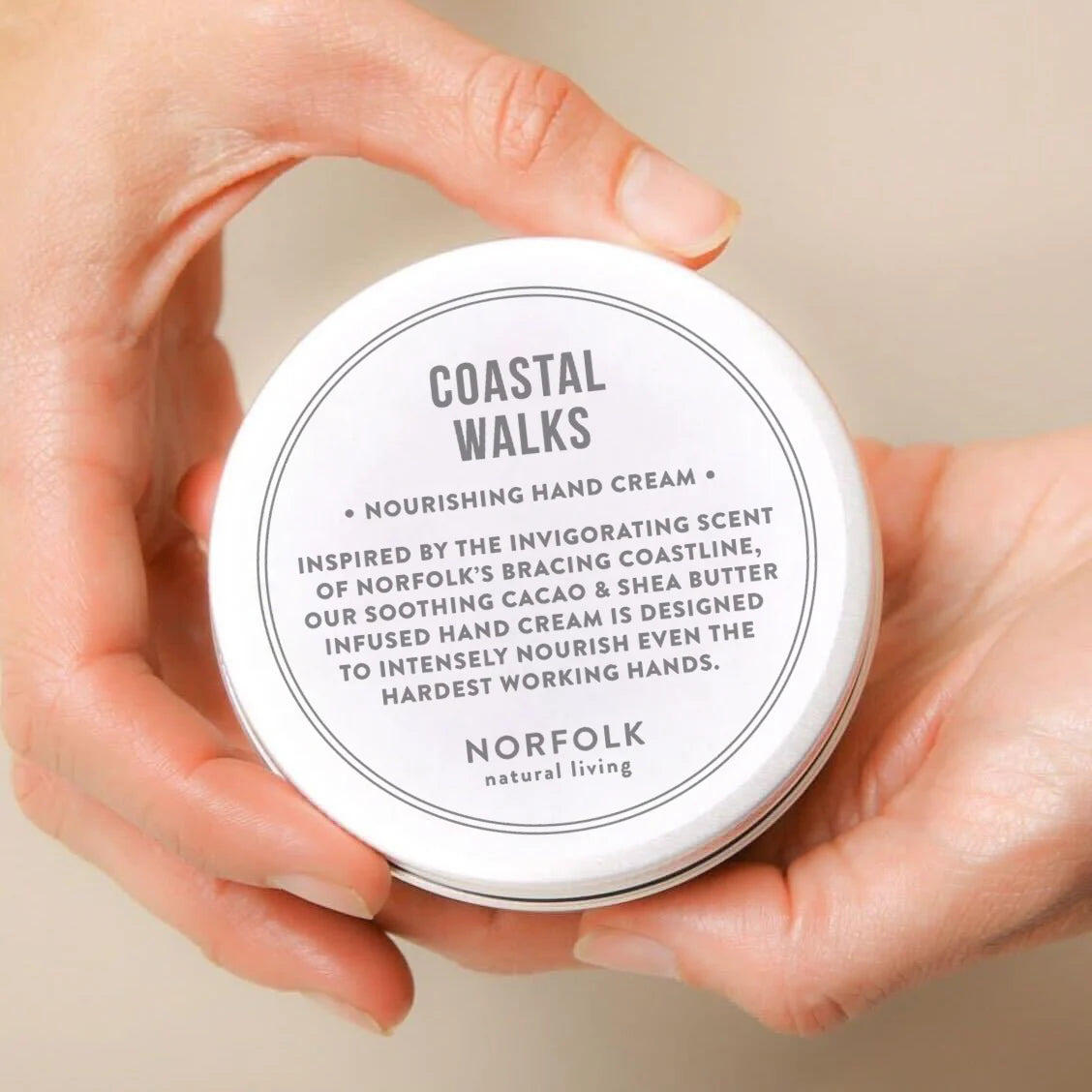 Hands holding a tin of Norfolk Natural Living Coastal Walks hand cream
