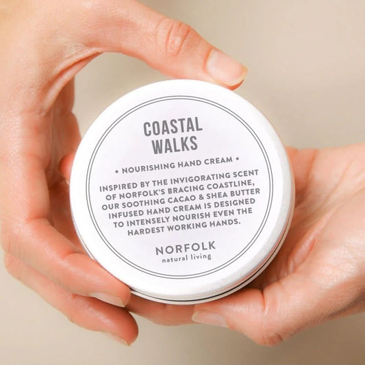 Hands holding a tin of Norfolk Natural Living Coastal Walks hand cream