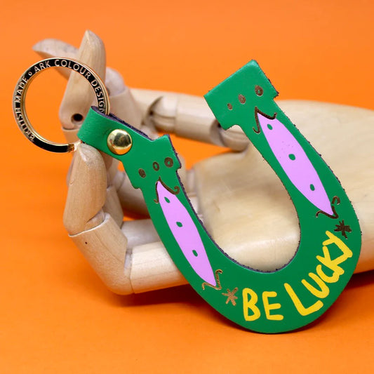 Ark green leather horseshoe key ring with 'Be lucky', held by a wooden hand
