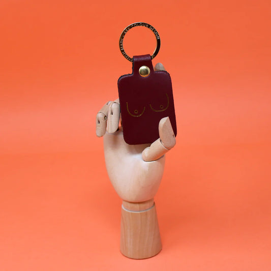 Oxblood leather key fob embossed with a pair of boobs, held by a wooden hand