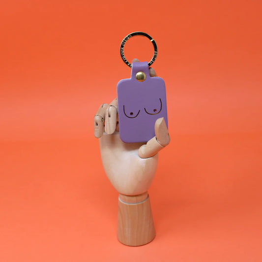 Lilac leather key fob printed with a pair of boobs, held by a wooden hand