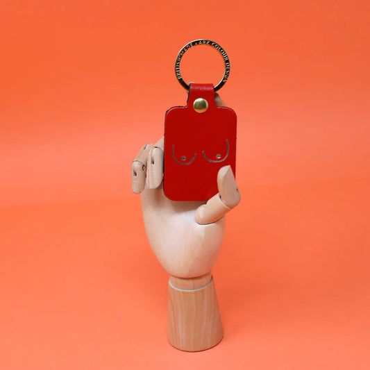 Red leather key fob embossed with a pair of boobs, held by a wooden hand