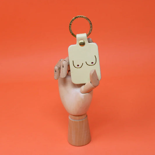 Cream leather key fob embossed with a pair of boobs, held by a wooden hand