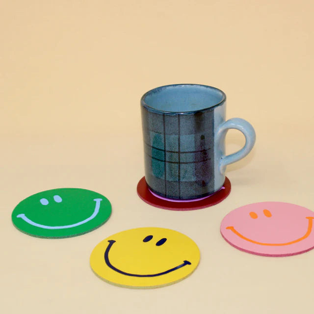 Smiley face leather coasters in green, yellow and pink, one under a mug